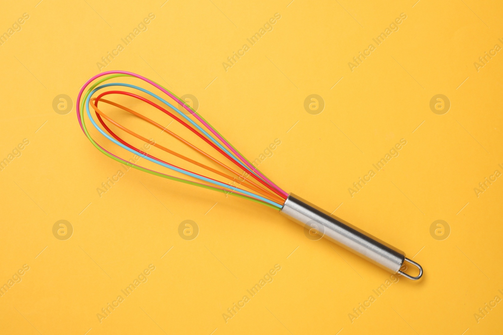 Photo of Bright whisk on yellow background, top view. Kitchen tool