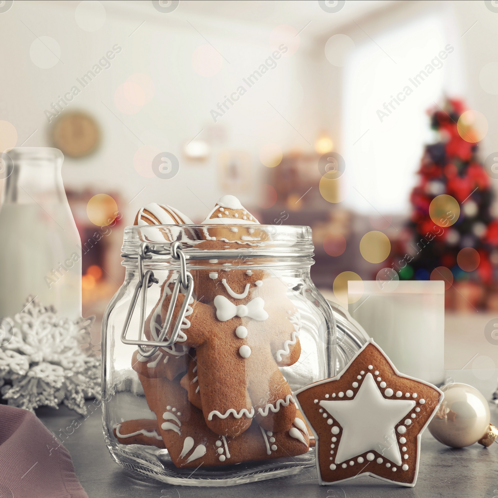 Image of Glass jar with Christmas cookies, milk and ornaments on table in decorated room 