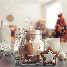 Image of Glass jar with Christmas cookies, milk and ornaments on table in decorated room 