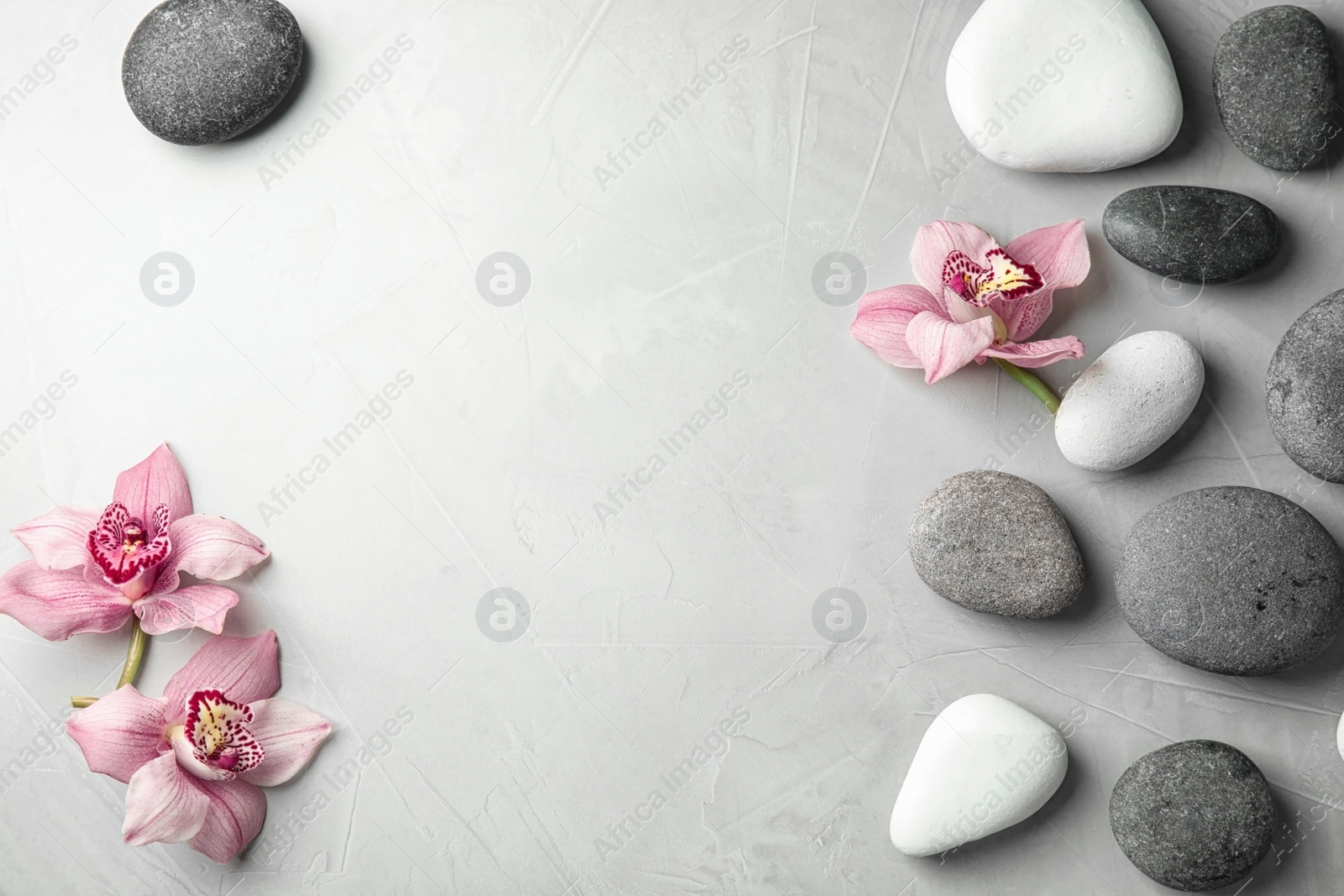 Photo of Zen stones and exotic flowers on grey background, top view with space for text