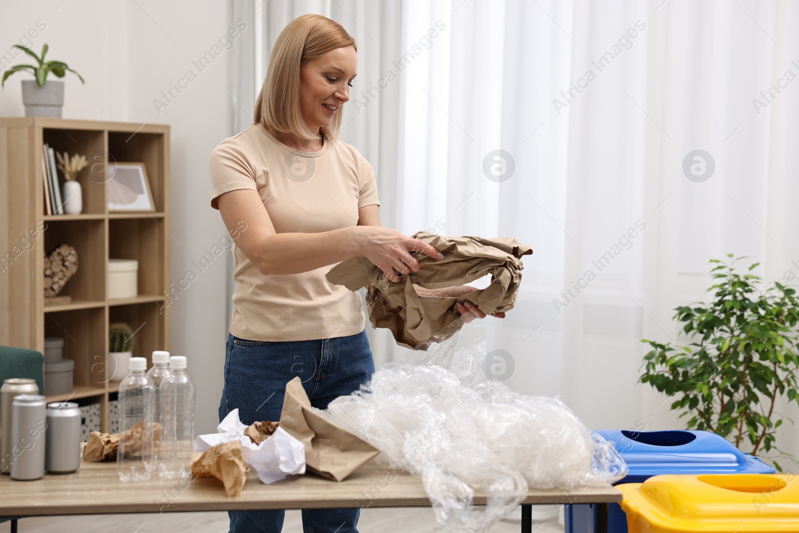 Photo of Smiling woman separating garbage in room. Space for text