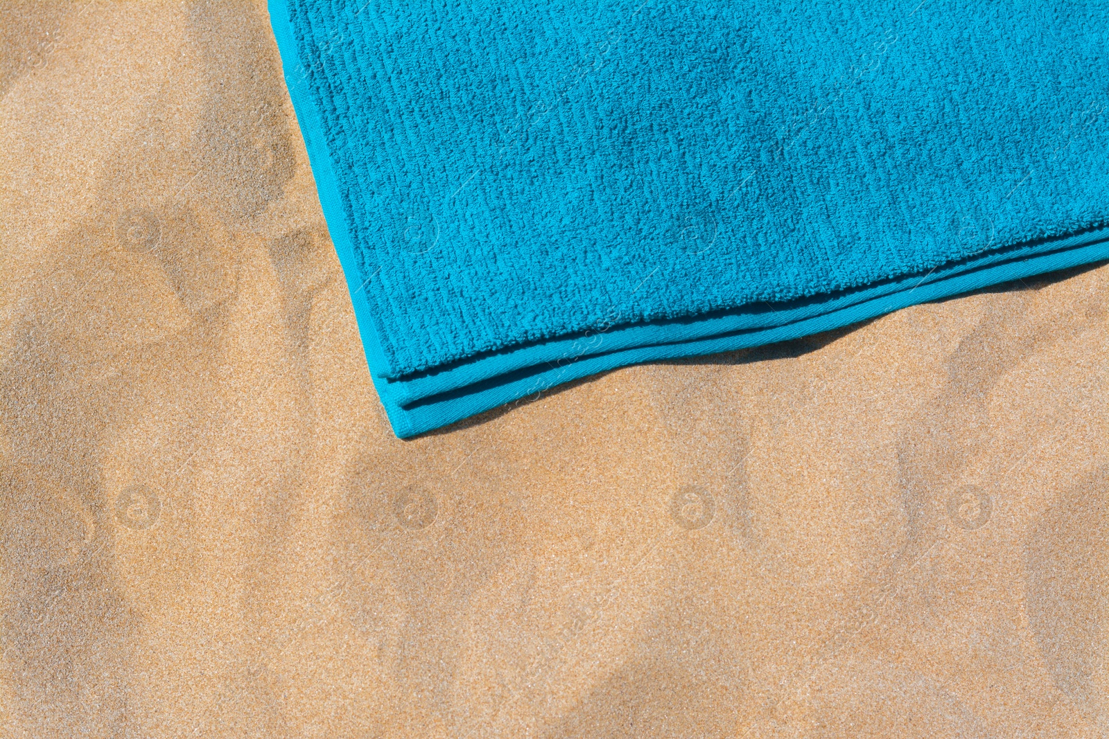 Photo of Soft blue beach towel on sand, above view. Space for text