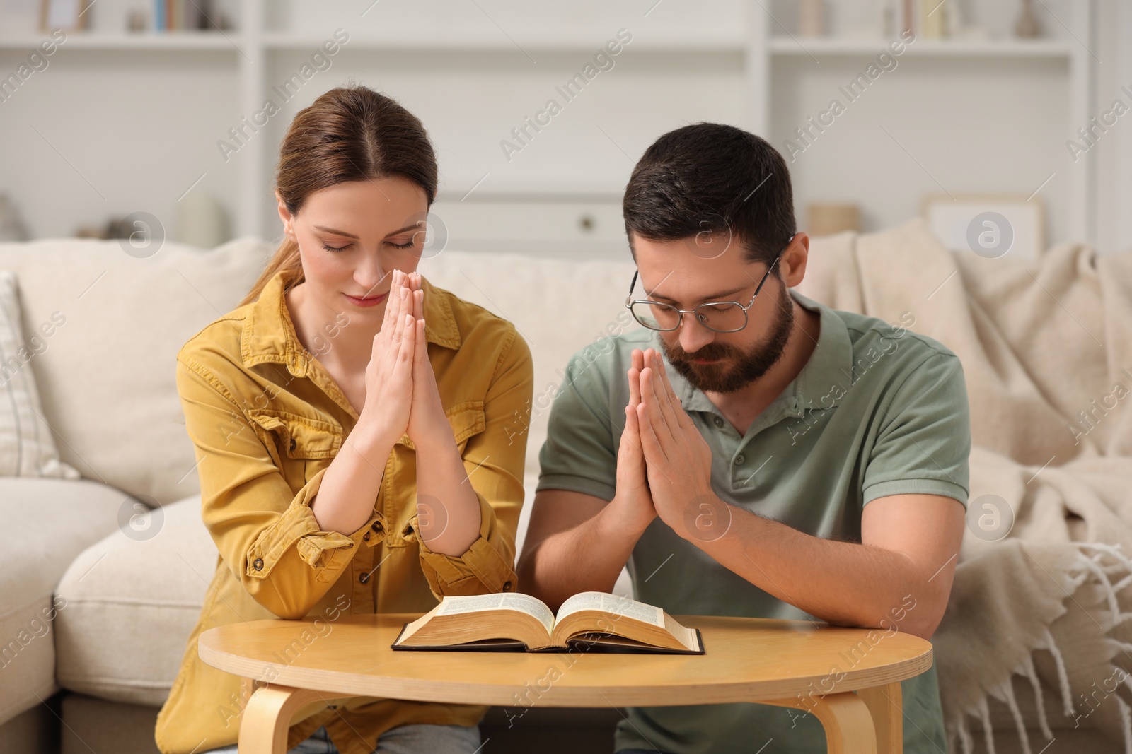 Photo of Family couple praying over Bible together at table indoors