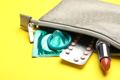 Photo of Cosmetic bag with contraceptives and red lipstick on yellow background, closeup. Safe sex concept