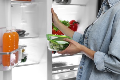 Photo of Young woman taking container with vegetables out of refrigerator, closeup