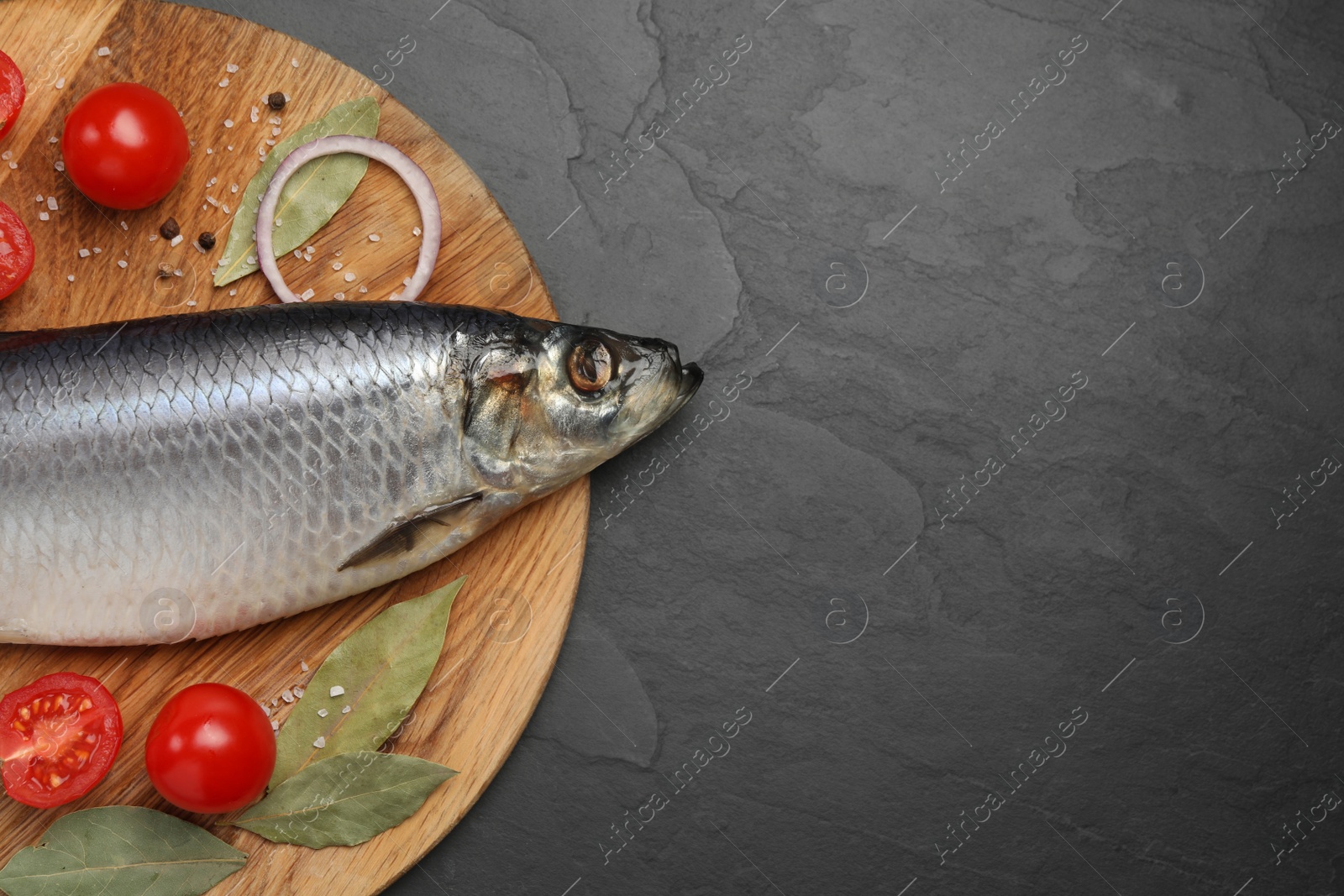 Photo of Tray with salted herring, onion, bay leaves and cherry tomatoes on black table, top view. Space for text