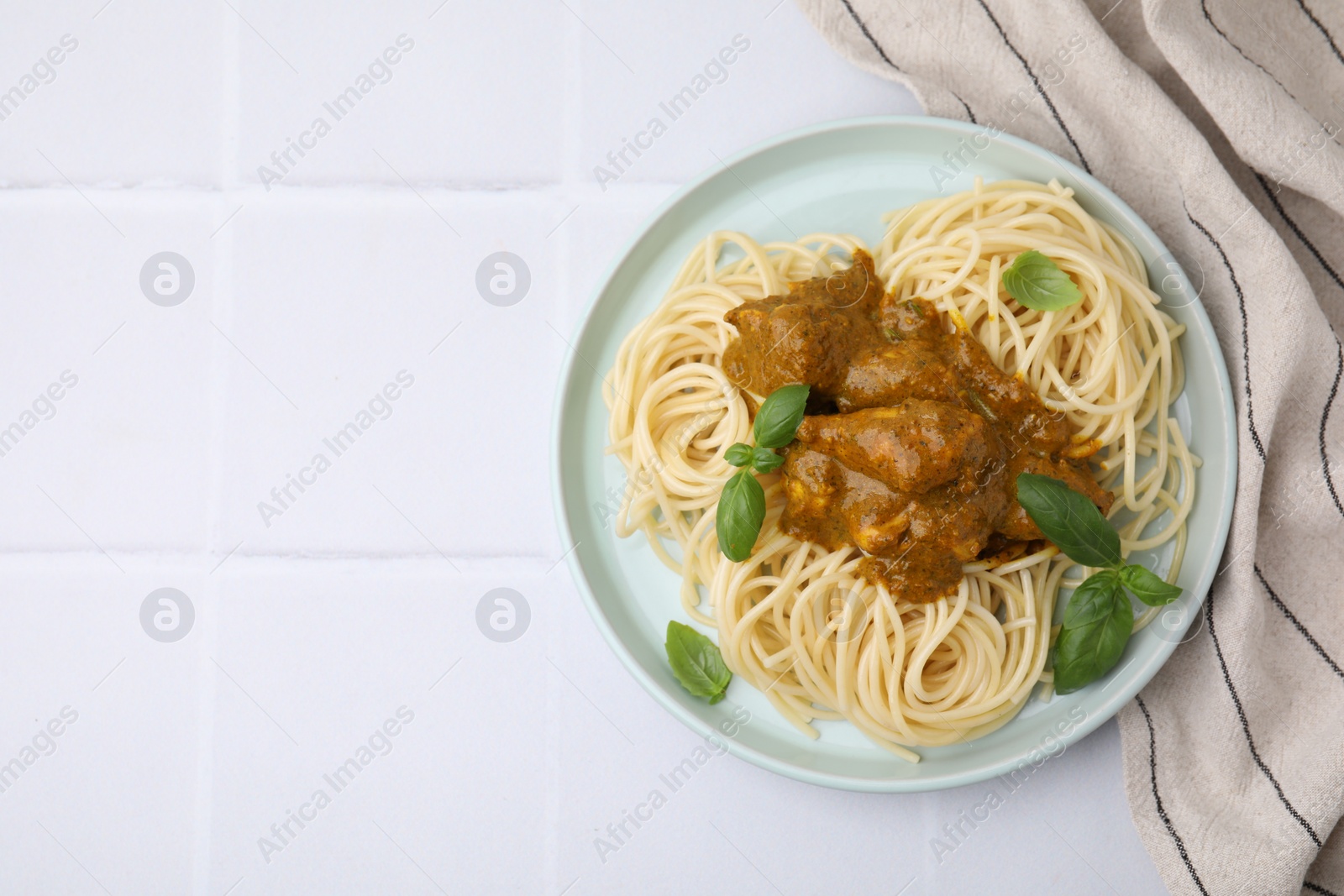 Photo of Delicious pasta and chicken with curry sauce on white tiled table, top view. Space for text