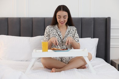 Happy young woman having breakfast on bed at home
