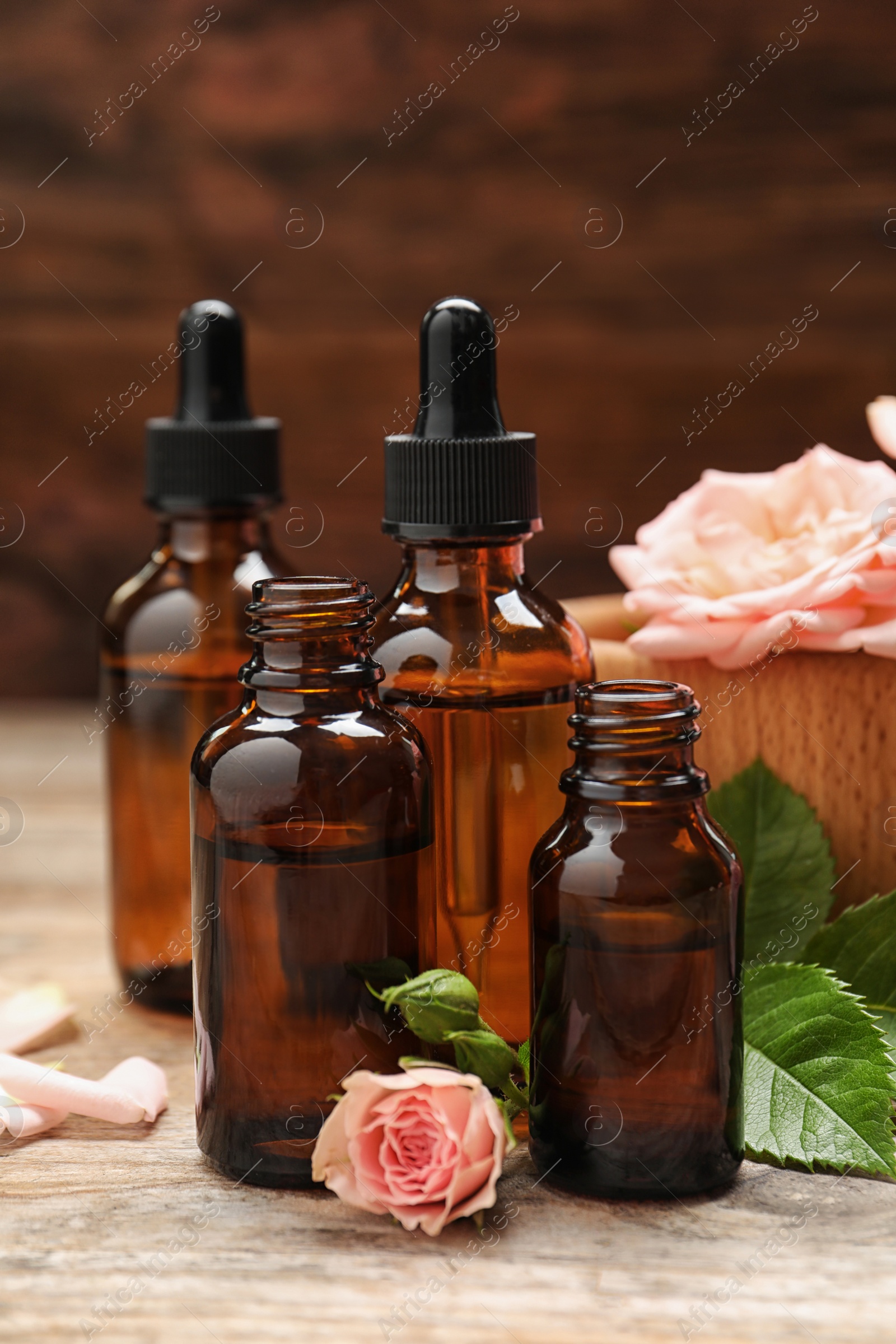 Photo of Bottles of rose essential oil and flowers on wooden table