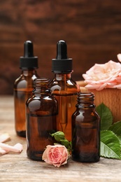 Photo of Bottles of rose essential oil and flowers on wooden table