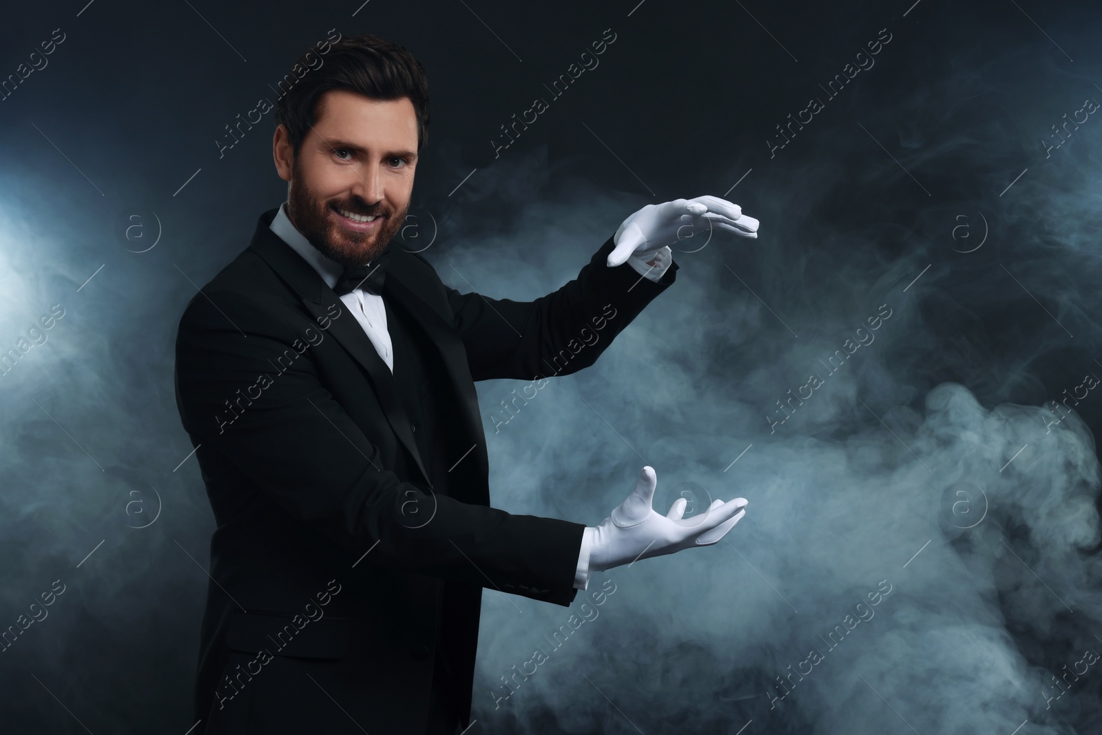 Photo of Happy magician holding something in smoke on dark background