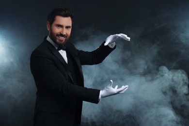 Photo of Happy magician holding something in smoke on dark background