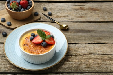 Photo of Delicious creme brulee with berries and mint in bowl on wooden table. Space for text