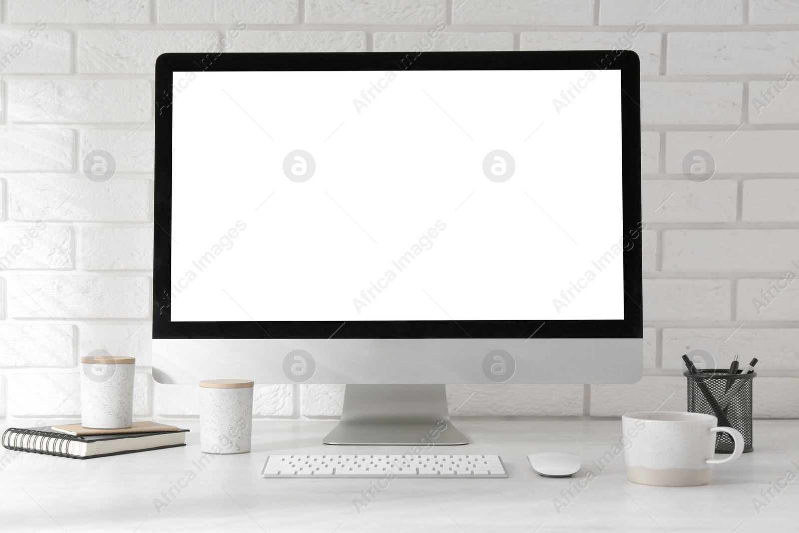 Photo of Office workplace with computer, cup and stationery on light table near white brick wall