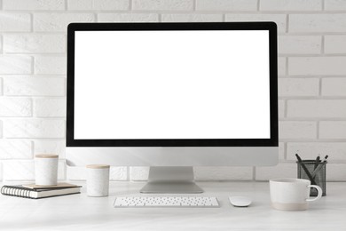 Photo of Office workplace with computer, cup and stationery on light table near white brick wall