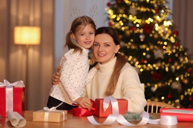 Photo of Christmas presents wrapping. Mother and her little daughter at table with gift boxes, decor in room