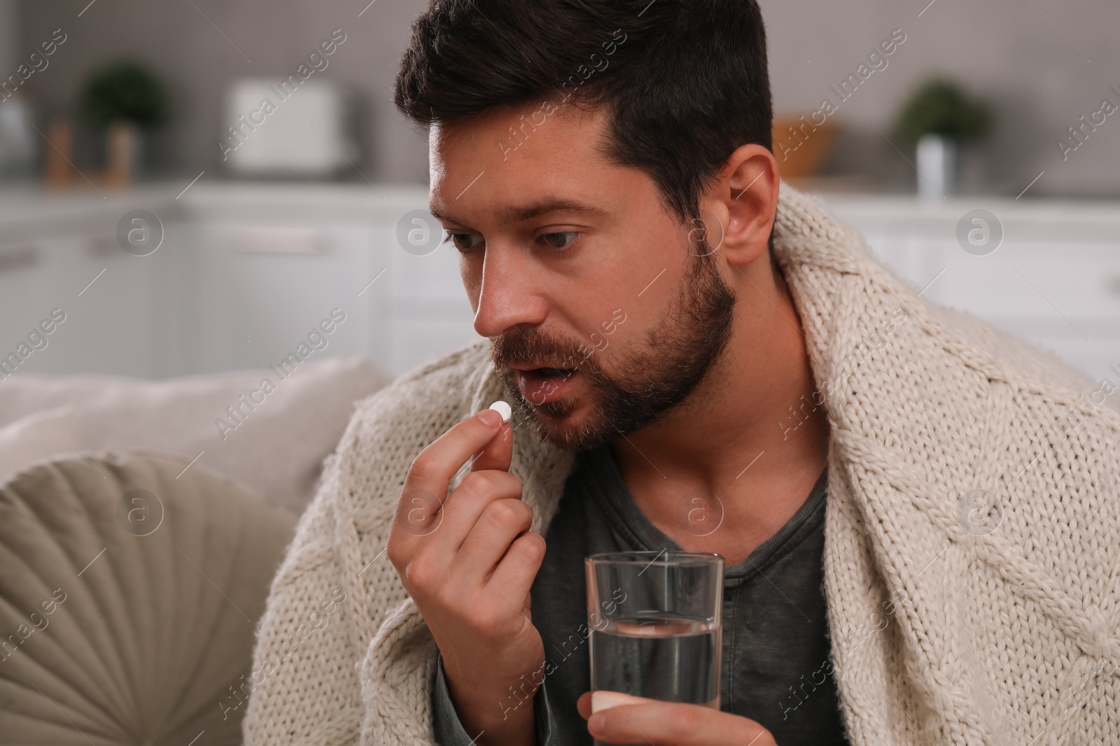 Photo of Depressed man with glass of water taking antidepressant pill indoors