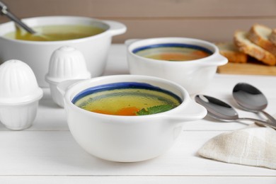 Photo of Delicious chicken bouillon with carrot and parsley on white wooden table, closeup