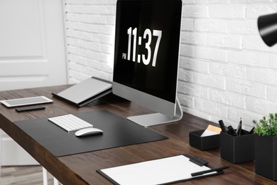 Modern workplace interior with computer and devices on table near brick wall