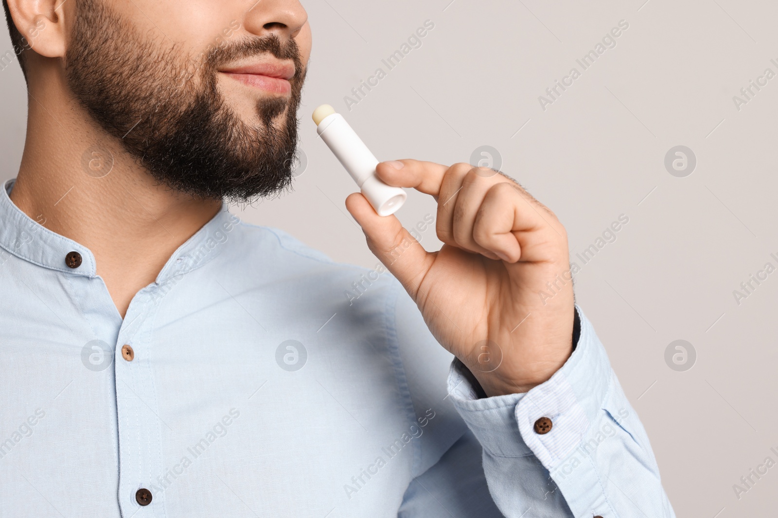 Photo of Young man applying lip balm on grey background, closeup