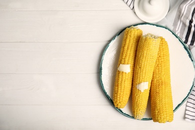 Photo of Fresh corn cobs with butter on white wooden table, flat lay. Space for text