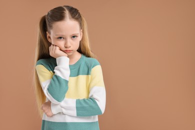 Portrait of sad girl on light brown background, space for text