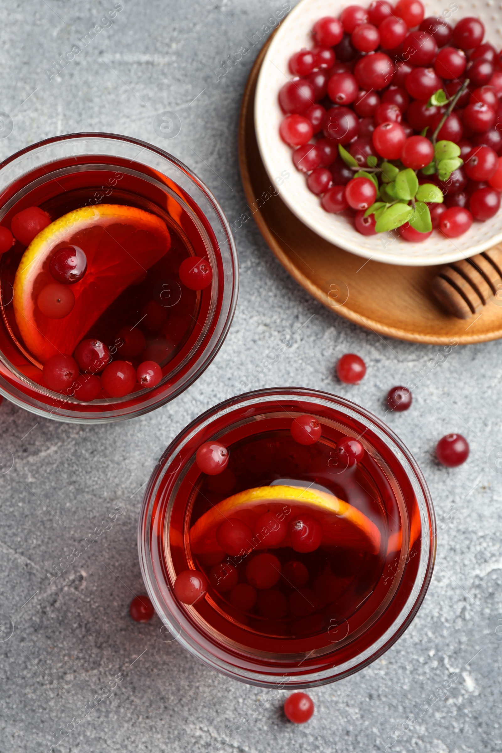 Photo of Tasty hot cranberry tea with lemon in glasses and fresh berries on light grey textured table