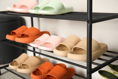 Photo of Shoe rack with different pairs of rubber slippers near white wall indoors, closeup