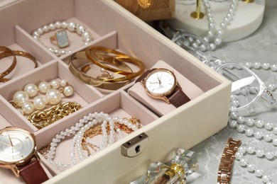 Jewelry box with many different accessories and perfume on light grey table, closeup