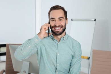 Young man laughing while talking on phone in office