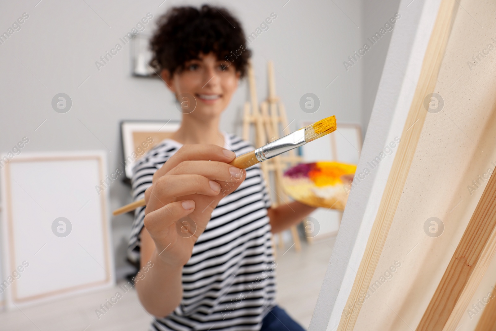 Photo of Young woman painting on easel with canvas in studio, selective focus