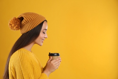 Happy beautiful woman with paper cup of mulled wine on yellow background. Space for text