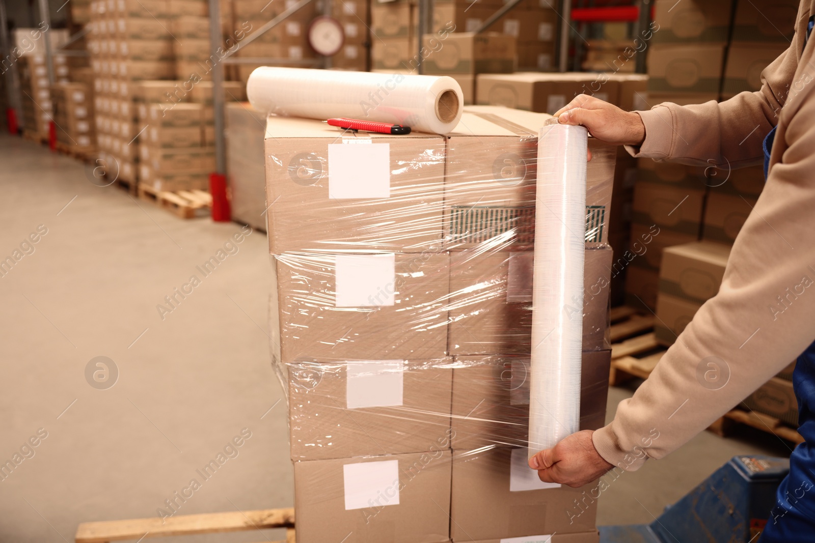 Photo of Worker wrapping boxes in stretch film at warehouse, closeup