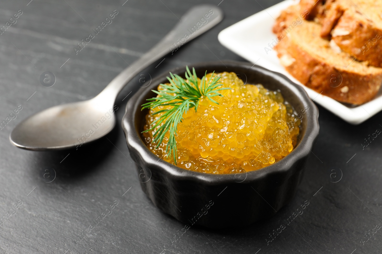 Photo of Fresh pike caviar in bowl, spoon and bread on black table