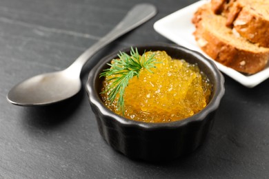 Fresh pike caviar in bowl, spoon and bread on black table