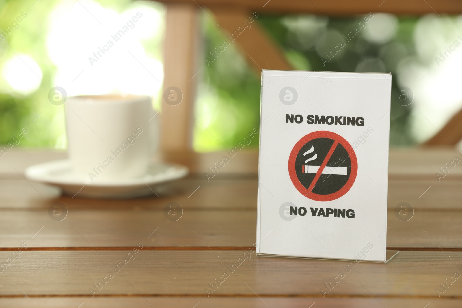 Photo of No Smoking No Vaping sign and cup of drink on wooden table outdoors. Space for text