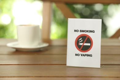 No Smoking No Vaping sign and cup of drink on wooden table outdoors. Space for text