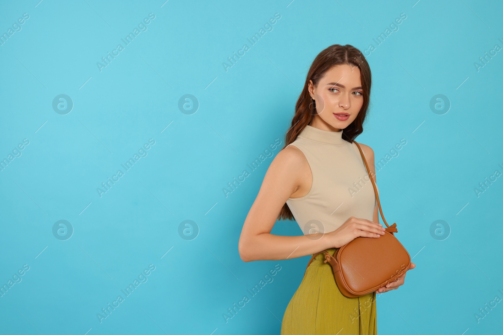 Photo of Beautiful young woman in fashionable outfit with stylish bag on light blue background, space for text