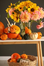 Photo of Autumn composition with beautiful flowers and pumpkins on console table near dark grey wall