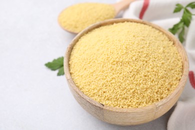 Raw couscous in bowl on light table, closeup