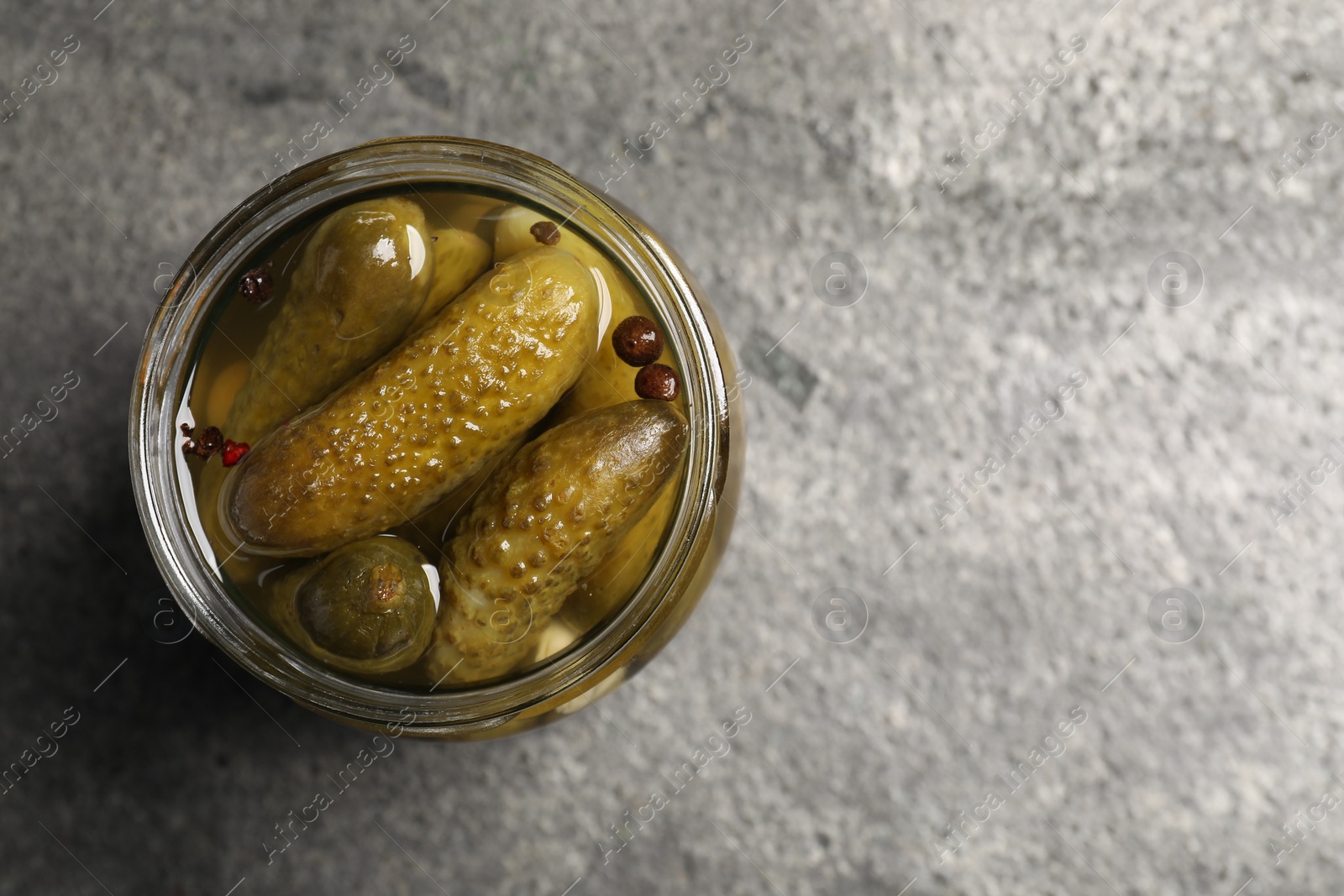 Photo of Tasty pickled cucumbers in glass jar on grey table, top view. Space for text