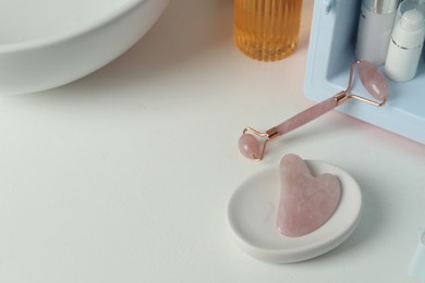 Photo of Rose quartz gua sha tool, natural face roller and cosmetic products on white table. Space for text