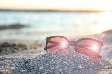 Photo of Stylish sunglasses on sandy beach at sunset