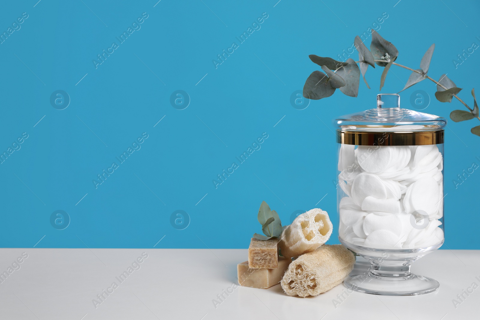 Photo of Jar with cotton pads on white table against blue background. Space for text