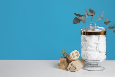 Jar with cotton pads on white table against blue background. Space for text