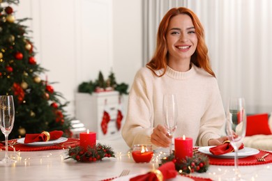 Beautiful young woman setting table in room decorated for Christmas