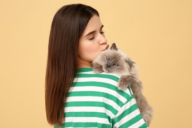 Woman kissing her cute cat on light brown background