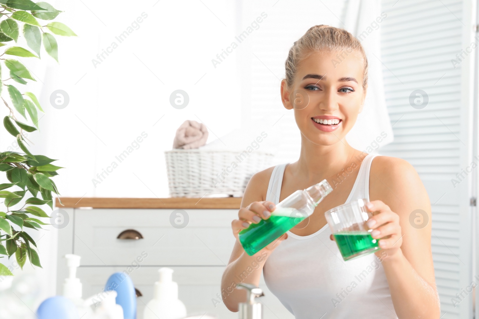 Photo of Woman pouring mouthwash from bottle into glass in bathroom. Teeth care