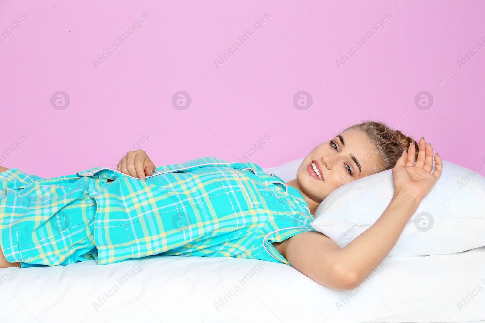 Photo of Beautiful woman lying with comfortable pillow on bed against color background