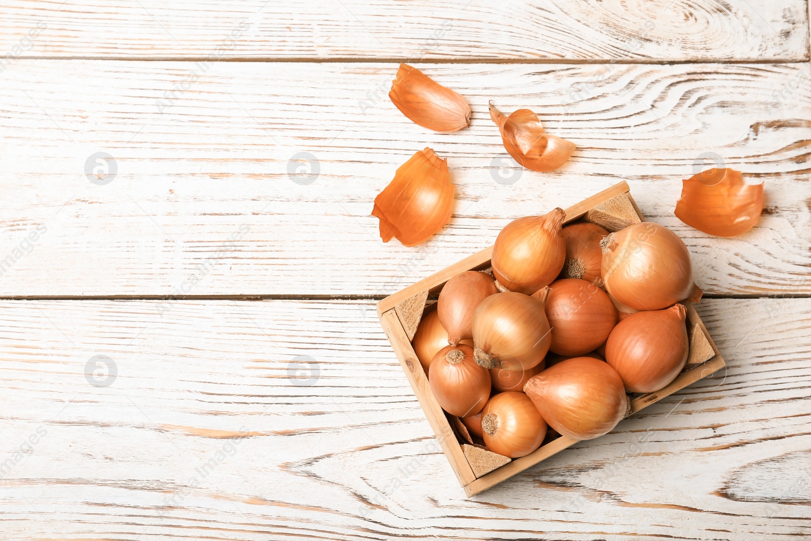 Photo of Crate with fresh ripe onions on wooden table, top view